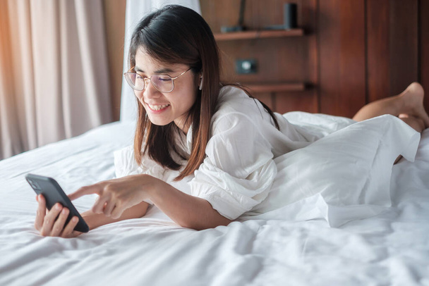 nő használ okostelefon a közösségi média, fiatal nő néz filmeket mobiltelefonnal az ágyon otthon. technológia, hálózat, online vásárlás, e-kereskedelem, életmód és digitális kommunikációs koncepció - Fotó, kép