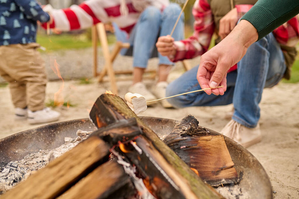 Male hand holding marshmallows on skewer over bonfire - Foto, afbeelding