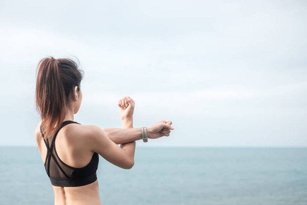Spor kıyafetli genç bir kadın, vücudu okyanus manzarasına karşı esnetiyor, sabahları sağlıklı kadın egzersizi yapıyor. Spor, sağlık ve iş hayatı dengesi kavramları - Fotoğraf, Görsel