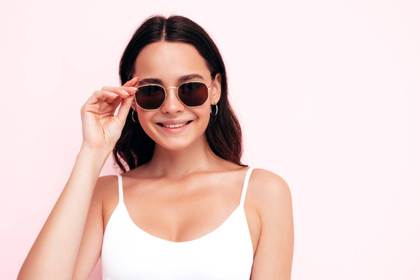 Closeup portrait of young beautiful smiling female in trendy summer clothes. Sexy carefree woman posing near pink wall in studio. Positive model having fun indoors. Taking off sunglasses - Φωτογραφία, εικόνα