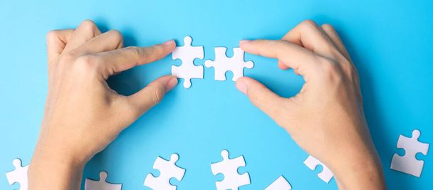 hands connecting couple white puzzle jigsaw pieces on blue background. Concept of solutions, mission, success, goals, cooperation, partnership, strategy and puzzle day - Photo, Image