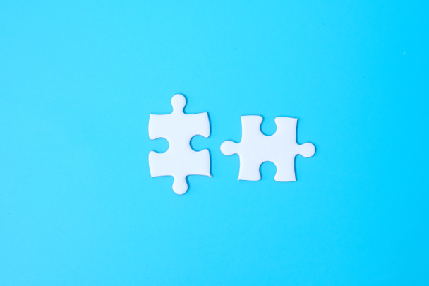 couple of white puzzle jigsaw pieces on blue background. Concept of solutions, mission, success, goals, cooperation, partnership, strategy and puzzle day - Фото, зображення