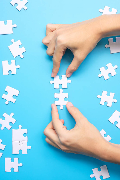 Hände, die ein paar weiße Puzzleteile auf blauem Hintergrund verbinden. Lösungskonzept, Mission, Erfolg, Ziele, Zusammenarbeit, Partnerschaft, Strategie und Puzzletag - Foto, Bild