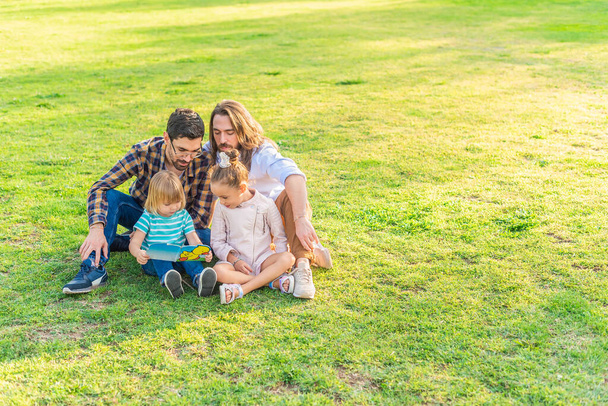 гей-чоловік пара зі своїми прийомними дітьми сидить на траві
 - Фото, зображення
