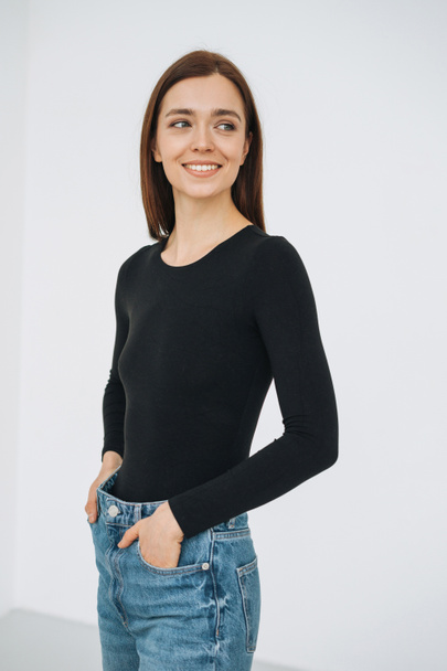Vertical portrait of happy young beautiful woman with dark long hair in black longsleeve and jeans in full length on white background isolated - Foto, immagini