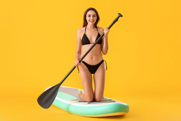 Junge Frau mit Surfbrett und Ruder auf farbigem Hintergrund - Foto, Bild