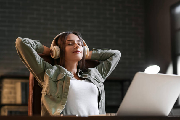 Mooie jonge vrouw met laptop luisteren naar muziek en ontspannen thuis in de avond - Foto, afbeelding