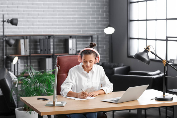 Pretty young woman listening to music while working in office - Photo, Image