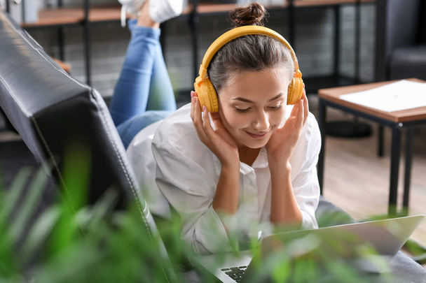Csinos fiatal nő laptoppal zenét hallgat otthon - Fotó, kép