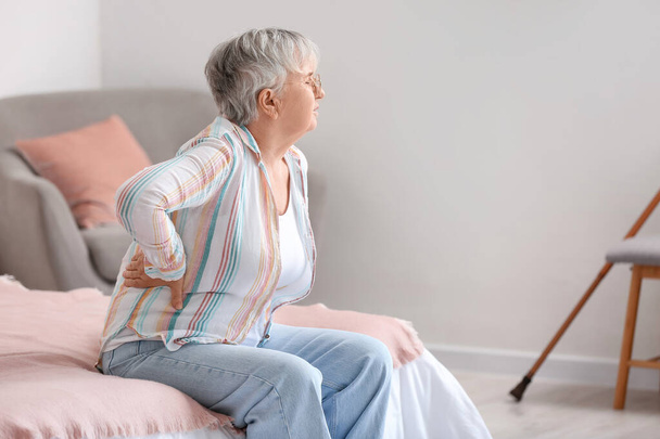 Oudere vrouw die last heeft van rugpijn op bed thuis - Foto, afbeelding