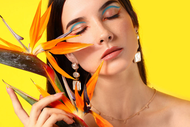 Beautiful young woman with strelitzia flowers on color background - 写真・画像