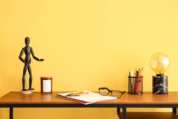 Modern workplace with stationery supplies, eyeglasses, lamp and mannequin doll near color wall - 写真・画像