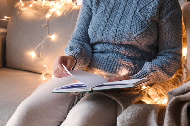 Woman reading book on sofa with glowing lights, closeup - Foto, immagini