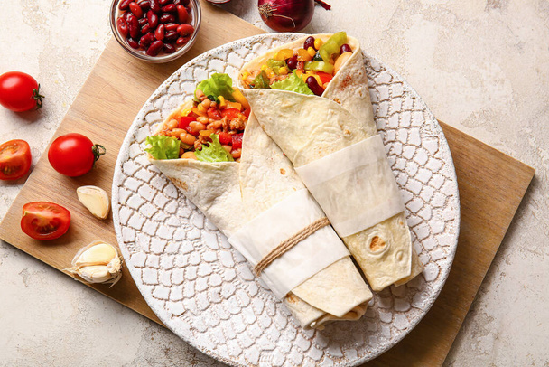 Plate with delicious burritos and ingredients on light background - Foto, Bild