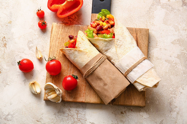 Board with delicious burritos and vegetables on light background - Фото, зображення