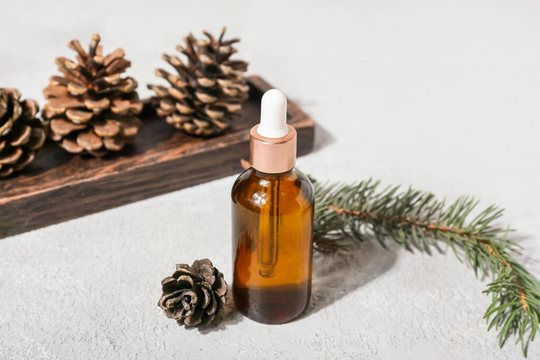 Bottle with essential oil, fir branch and pine cones on light background - Foto, immagini