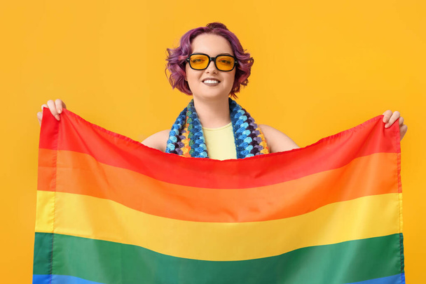 Sarı arka planda LGBT bayrağı olan genç bir kadın. - Fotoğraf, Görsel