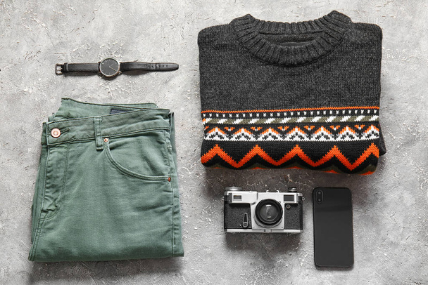Mannelijke trui, broek, polshorloge, fotocamera en mobiele telefoon op grunge achtergrond - Foto, afbeelding