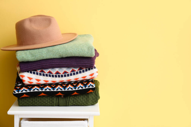 Stack of stylish sweaters and felt hat on stool near color wall - Foto, imagen