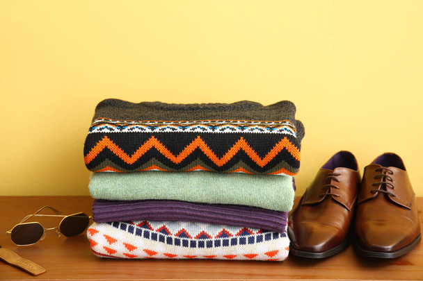 Stack of stylish sweaters, accessories and shoes on table near color wall - Foto, Imagem
