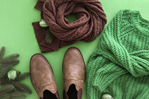 Knitted sweater, scarf, shoes and Christmas decor on green background, closeup - Fotó, kép