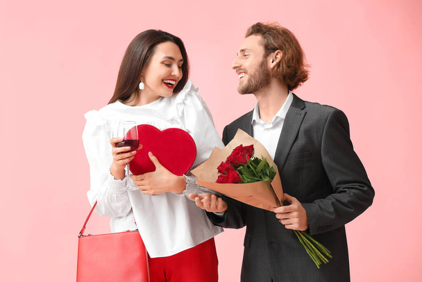 Happy young couple with wine, gift and flowers on color background. Valentine's Day celebration - Photo, Image