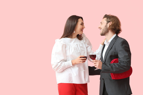 Happy young couple with wine and gift on color background. Valentine's Day celebration - Foto, imagen