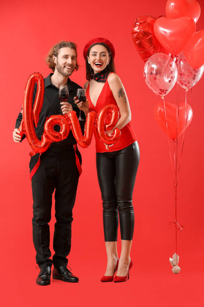 Happy young couple with wine and balloons on color background. Valentine's Day celebration - Fotó, kép