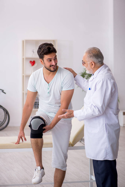 Genç bacağı yaralı hasta yaşlı doktoru ziyaret ediyor. - Fotoğraf, Görsel