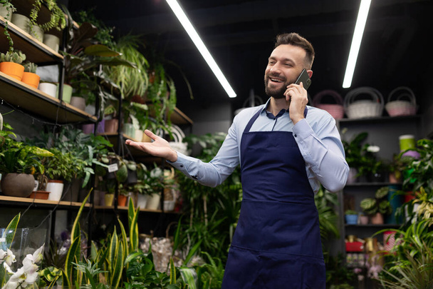 a florist in blue aprons in a potted plant and flower shop takes an order by phone for Valentines Day - Foto, Bild