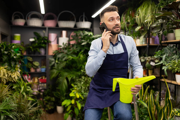 florist In the garden center, watering and caring for potted plants by talking on the phone - Photo, Image