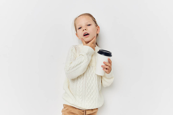 little girl in white sweater glass with drink light background - Фото, зображення