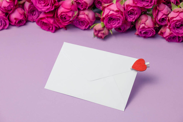 Envelope and rose flowers on violet background. Valentine's day greeting card.  - Zdjęcie, obraz