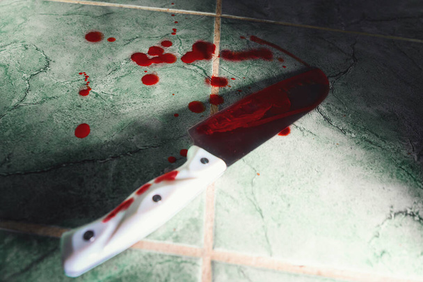 Στενή θέα ενός μεγάλου κοφτερού μαχαιριού με αίμα. Όπλο βρίσκεται στο πάτωμα επενδεδυμένο με πράσινα πλακάκια. Αντιγραφή χώρου. Η έννοια της βίας, του εγκλήματος και της δολοφονίας. - Φωτογραφία, εικόνα