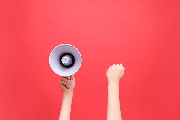 Close up of female hands holding megaphone and raised fist, political protest to showing his power, isolated on red studio background with copy space for your text or design. Concept revolution, fight - Фото, изображение