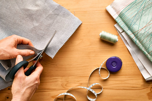 Vrouwenhanden snijden een patroonpapier uit in linnen stof. Naaister naaien op naaimachine in kleine studio. Fashion atelier, maatwerk, handgemaakte kleding concept. Trage mode Bewust verbruik - Foto, afbeelding