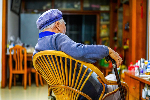 Evdeki sandalyede dinlenen yaşlı bir adam. - Fotoğraf, Görsel