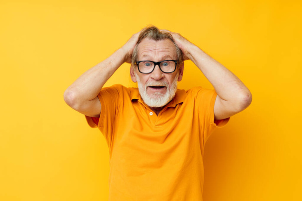 Senior grey-haired man posing yellow tshirt glasses yellow background - Foto, Imagem