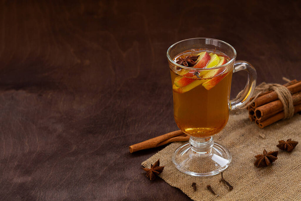 glass of mulled wine with spices. homemade spice apple cider with fresh apples, honey, cinnamon, cardamon, anise, clove. hot fruit tea on the wooden table. Christmas drinks. traditional hot autumn drink. cope space. - Photo, Image