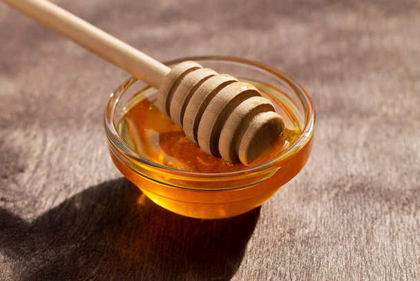 glass bowl of honey with wooden dipper on the wooden table. Close-up. Healthy organic thick honey. copy space - Photo, Image
