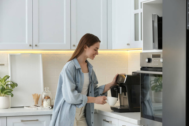 Young woman preparing fresh aromatic coffee with modern machine in kitchen - 写真・画像