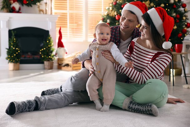 Happy family with cute baby on floor in room decorated for Christmas - Фото, изображение