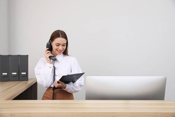 Female receptionist with clipboard talking on phone at workplace. Space for text - Photo, Image