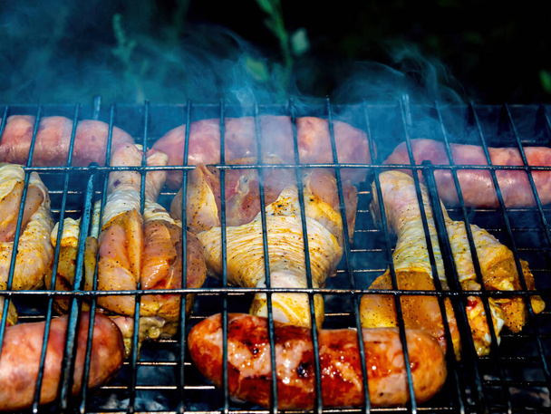 Patas de pollo y salchichas de carne en una red de barbacoa de hierro sobre el fuego. - Foto, imagen