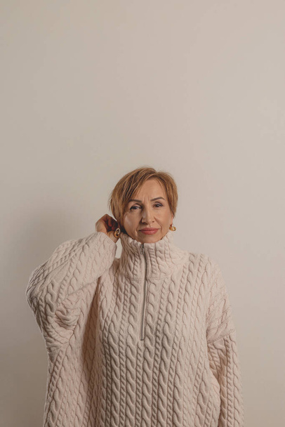 Beautiful middle-aged baby boomer woman in beige sweater on neutral background. - Photo, Image