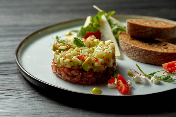 Delicious salmon tartare with avocado and croutons on a plate. wood background. Selective focus - 写真・画像