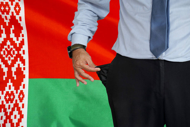 Close-up of hand of man in suit turning pocket of his trousers inside out and showing it empty on the background of the Belarus flag. Crisis, unemployment, bankruptcy concept in Belarus - Фото, изображение