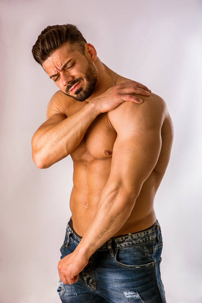 Muscular man holding his shoulder with one hand and grimacing in pain - Foto, Imagen