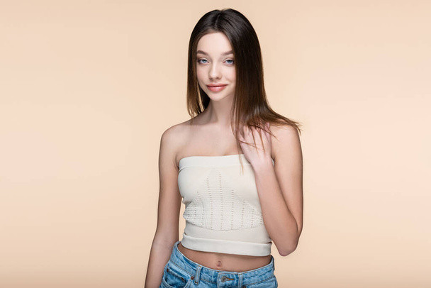 pleased young woman in crop top with bare shoulders isolated on beige - Valokuva, kuva
