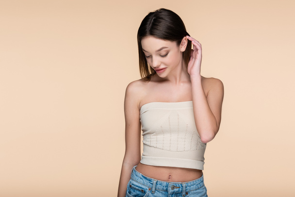 young and shy woman in crop top with bare shoulders isolated on beige  - Foto, Imagem